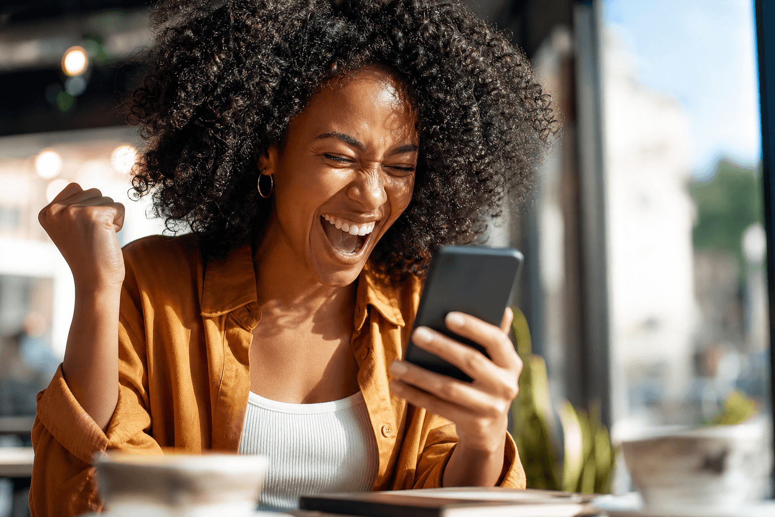 Happy professional celebrating a job offer on her phone in a coffee shop